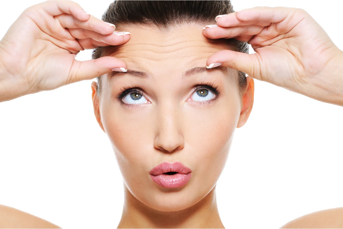 Woman lifting eyebrows to show deep forehead furrows and expression lines for wrinkle reduction treatment at Outer Banks Dermatology.